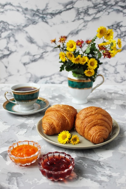 Frans ontbijt met croissants, abrikozenjam, kersenjam en een kopje thee, rode en gele bloemen