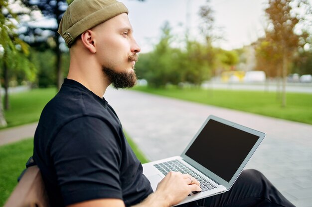 Freelancer met laptop zit in het stadspark terwijl blogger hipster reiziger jonge stijlvolle man werkt