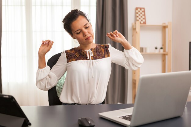 Freelancer met zere rug tijdens het werken op laptop vanuit thuiskantoor.