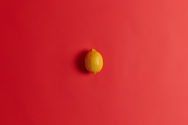 Frisse gele zure citroen rijk aan vitamine C, foliumzuur, vezels en kalium om uw immuniteit te versterken, verkoudheid of griep te genezen. Sappige sappige tropische citrusvruchten geïsoleerd op een rode achtergrond.