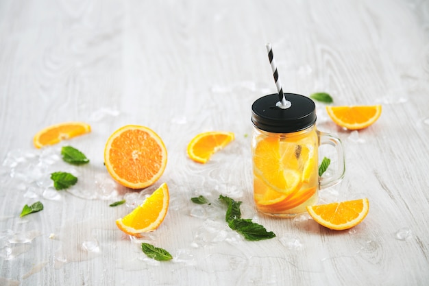 Frisse koude zomer limonade van citrus en bruisend water in rustieke pot met stro van streep geïsoleerd op houten tafel.