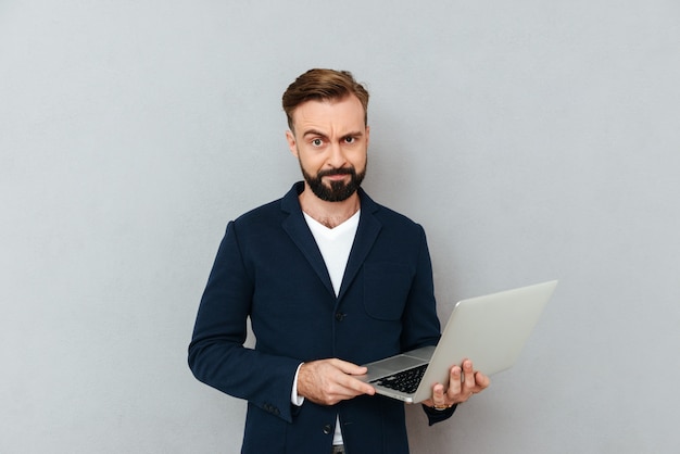 Frons ernstige mens in kostuum dat geïsoleerde laptop met behulp van