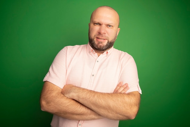 Fronsen kale man van middelbare leeftijd met roze t-shirt handen kruisen