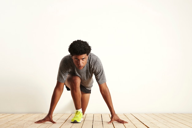 Front shot van een gefocuste fit runner die grijs, zwart en geel draagt in de uitgangspositie, klaar om te beginnen met rennen op wit