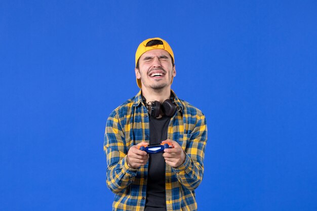 Front view van een mannelijke gamer met een gamepad die een videospel speelt op een blauwe muur