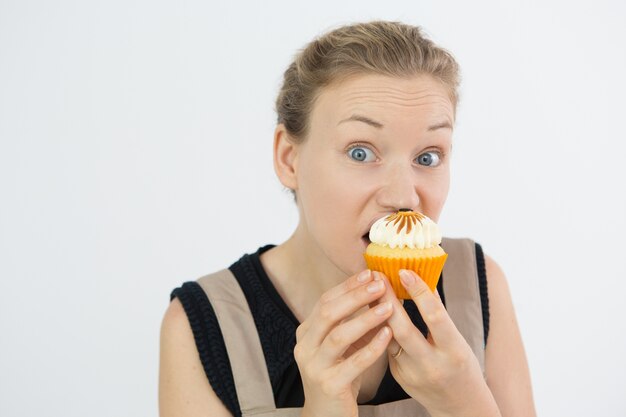 Frowning jonge vrouw die cupcake met hebzucht eet