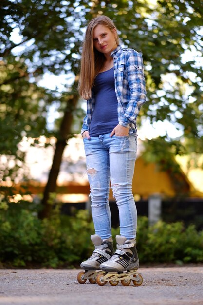 Full body portret van aantrekkelijke casual vrouw in rolschaatsen op een weg.