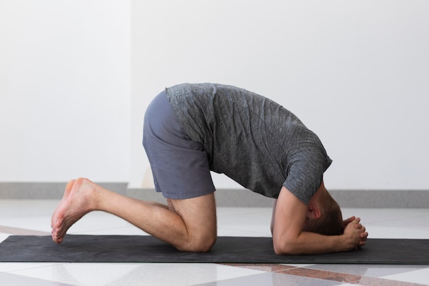 Full shot man doet yoga pose binnen