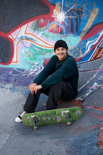 Gratis foto full shot smiley tiener zit in skatepark