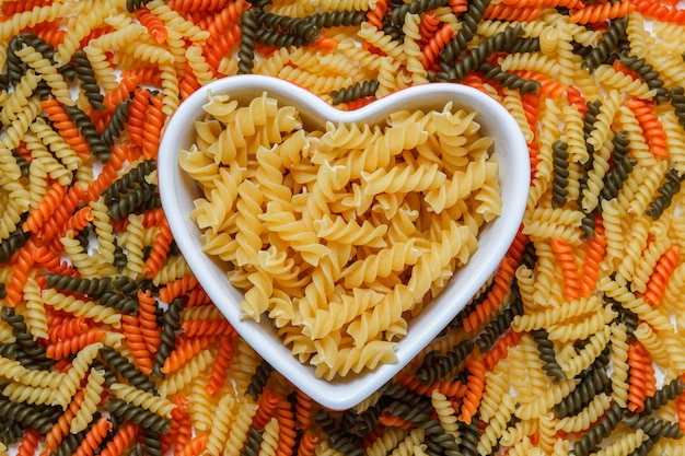 Fusilli pasta in een hartvormige kom op macaroni tafel, plat lag.