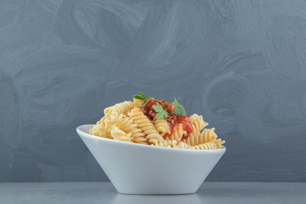 Fusilli pasta met ketchup in witte kom.