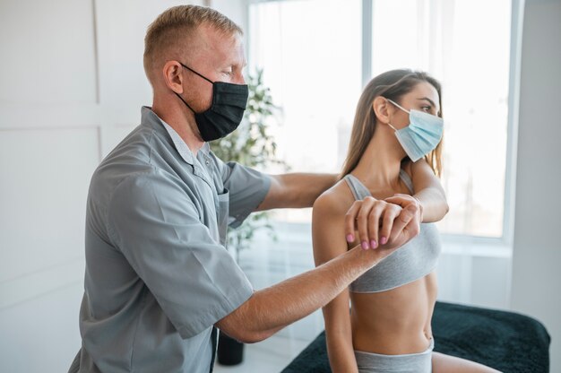 Fysiotherapeut die medische masker draagt tijdens een therapiesessie met vrouwelijke patiënt