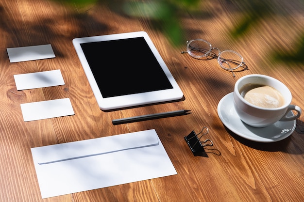 Gadgets, koffie, werktuigen op een houten tafel binnenshuis. Creatieve, gezellige werkplek op kantoor aan huis, inspirerende mock-up met plantschaduwen op het oppervlak. Concept van extern kantoor, freelance, sfeer.