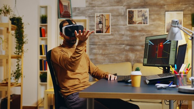 Gameontwikkelaar met virtual reality-headset die handgebaar maakt terwijl hij nieuwe graphics van de game maakt.