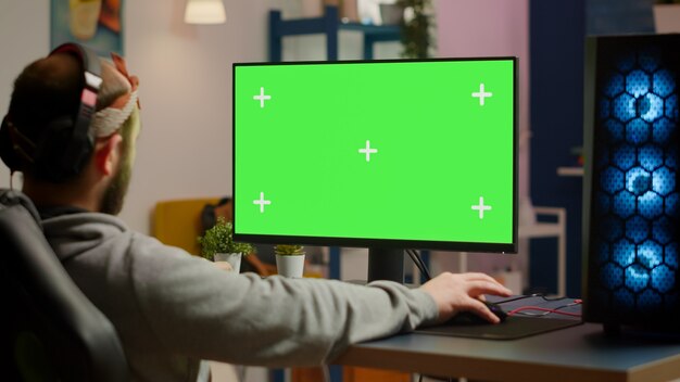 Gamer die videogames speelt op een krachtige computer met groen scherm chroma key desktop mock-up display in gaming home studio. Speler die RGB-toetsenbord gebruikt met een geïsoleerd monitor-streamingspel met een headse