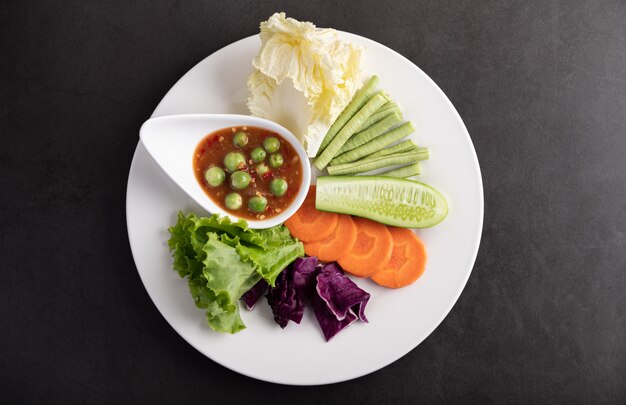 Garnalenpastasaus in een kom op de witte plaat met komkommer, kousenband, Thaise aubergine, gebakken witte kool, wortelen en salade