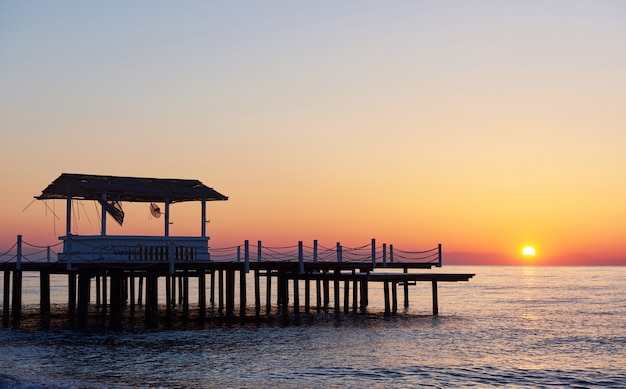 Gazebo op de houten pier in de zee met de zon bij zonsondergang.