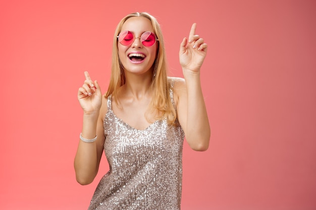 Geamuseerd aantrekkelijke gelukkig lachende vrouw dansen nachtclub plezier genieten van ga wild feest vieren b-dag dragen stijlvolle jurk zonnebril opsteken wijsvingers glimlachend meezingen