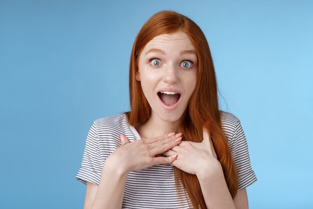 Geamuseerd, blij, dankbaar, europese roodharige vrouw hijgend naar beneden kaken, druk met vreugde op de handpalmen op de borst dankbaar staren verrast ongelooflijk cool cadeau ontvang geweldig voorstel staande blauwe achtergrond.