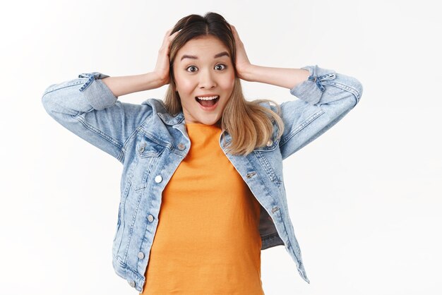 Geamuseerd blij schattig aziatisch blond meisje ontvangt geweldig spannend nieuws grijp hoofd glimlachend breed toothy opgewonden glimlach reageren geweldig geweldig positieve situatie staand witte achtergrond