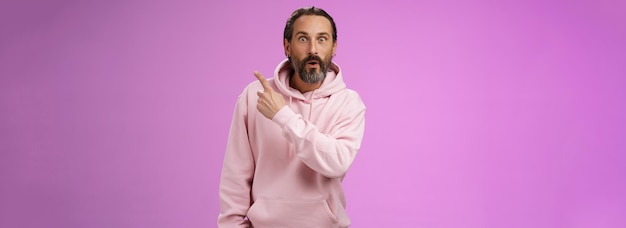 Gratis foto geamuseerde knappe hipster volwassen s bebaarde blanke man grijs haar met trendy roze hoodie vouwlip