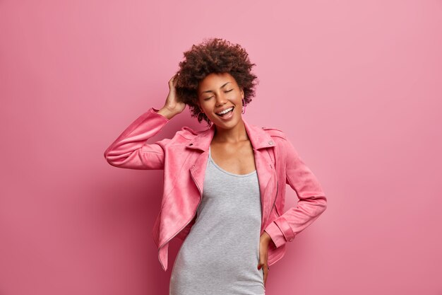 Geamuseerde zorgeloze jonge Afro-Amerikaanse vrouw met gesloten ogen, geniet van een geweldige vrije dag, gekleed in stijlvolle kleding, glimlacht breed