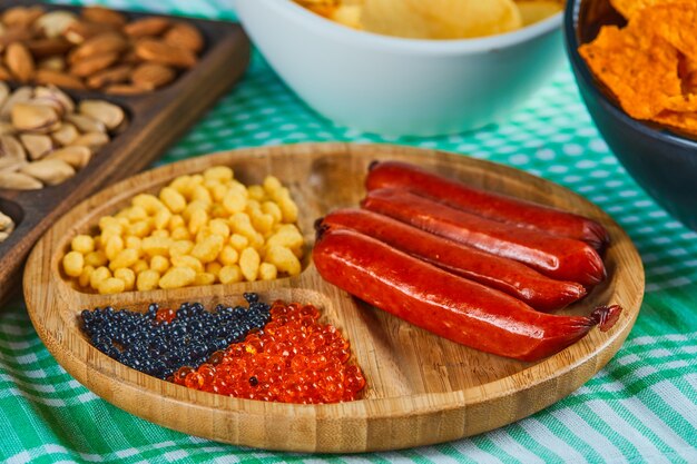 Geassorteerde snacks, kom chips en een bord worst op een blauwe tafel.