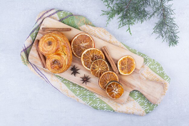 Gebak met kaneelstokjes, kruidnagel en sinaasappelen op een houten bord.