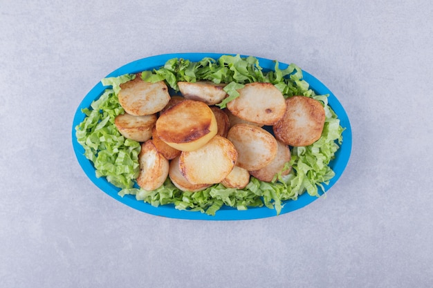 Gebakken aardappelen en sla op blauw bord.
