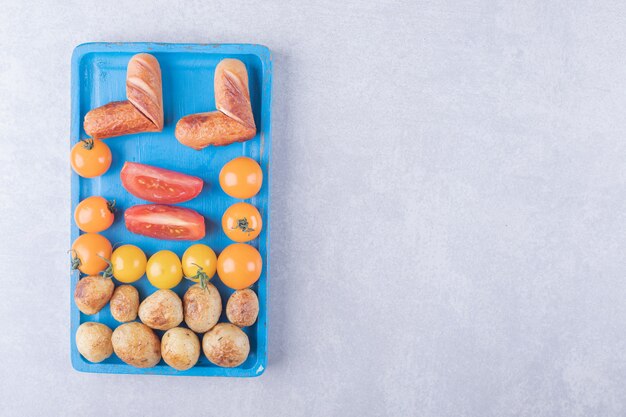 Gebakken aardappelen en worstjes op blauw bord.