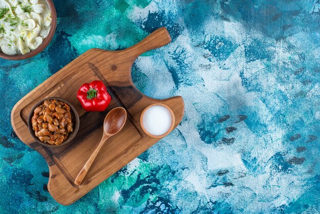 Gebakken bonen, dushbara, lepel, peper en zout op een bord, op de blauwe tafel.