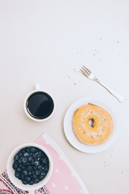 Gebakken donut; koffiekop; servet; vork en bosbessen op witte achtergrond