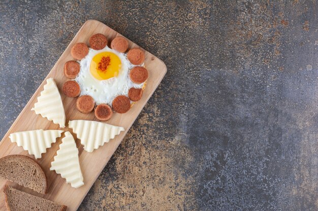 Gebakken ei met worstjes en plakjes kaas op een houten bord