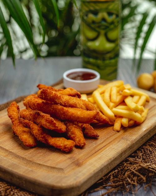 Gebakken gepaneerde kipfilet strips met ketchup en frietjes op een houten bord