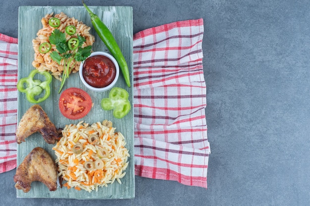 Gebakken kip met rijst en pasta op een houten bord.