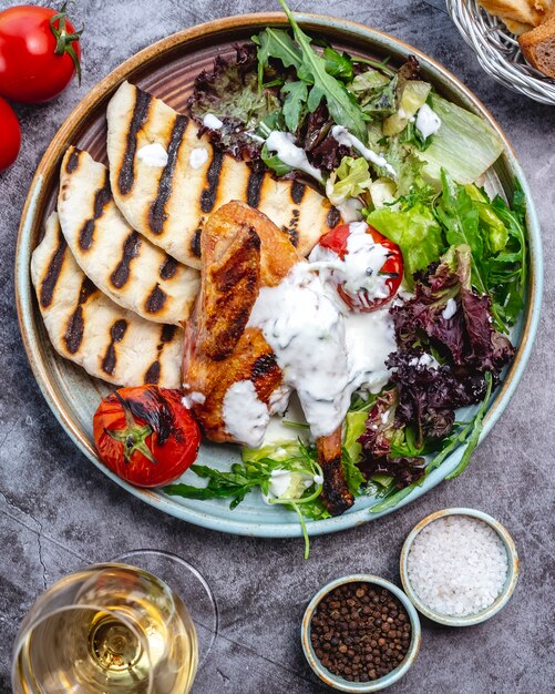 Gebakken kippenpoot gegarneerd met saus geserveerd met sla, rucola, gegrilde pita en tomaat