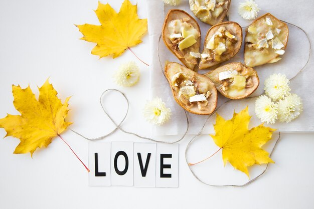 Gebakken peren met brie-kaas en noten tegen de achtergrond van gele herfstbladeren, inscriptie love