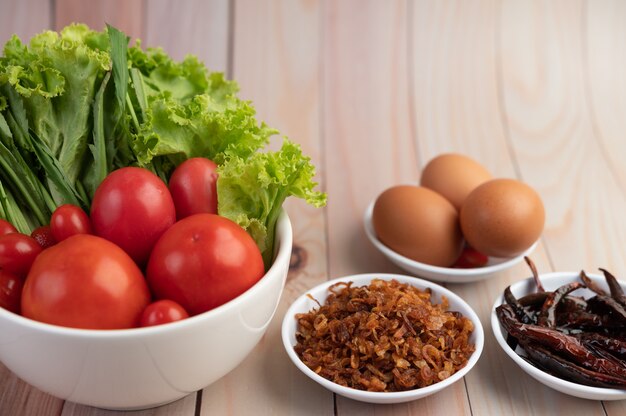Gebakken uien, paprika, eieren, tomaten, salade en lente-uitjes in een witte kop op een houten vloer.