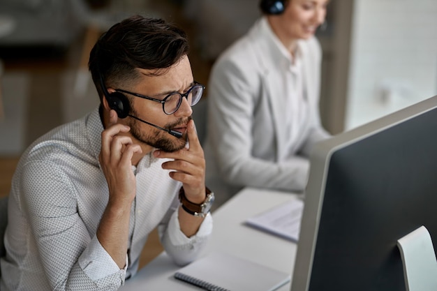 Geconcentreerde callcentermedewerker die met een klant praat terwijl hij op kantoor werkt