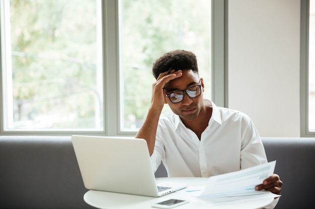 Geconcentreerde ernstige jonge Afrikaanse man zit coworking