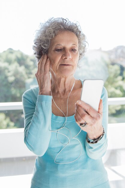 Geconcentreerde hogere dame die telefoon en oortelefoons gebruikt