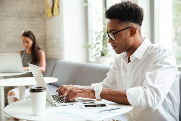 Geconcentreerde jonge Afrikaanse man zit coworking
