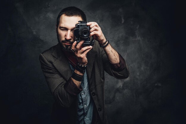 Geconcentreerde jonge fotograaf neemt een foto op de donkere grungeachtergrond.