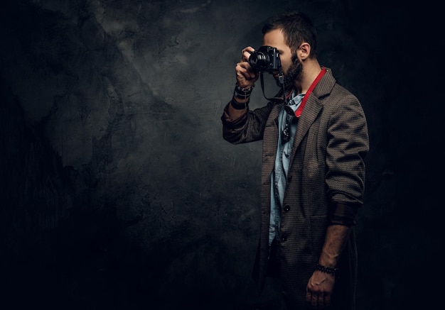 Geconcentreerde jonge fotograaf neemt een foto op de donkere grungeachtergrond.