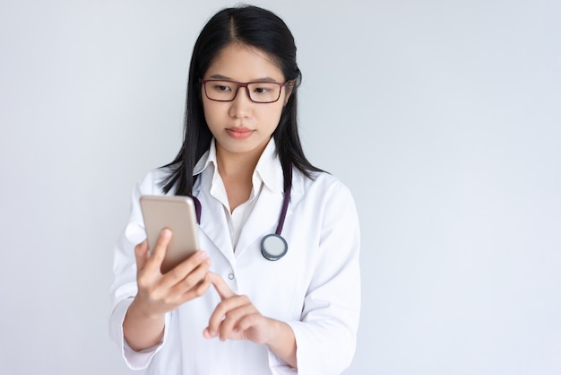 Geconcentreerde jonge vrouwelijke arts die smartphone gebruikt
