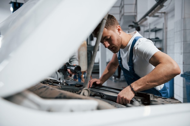 Geconcentreerde look. Werknemer in het blauw gekleurde uniform werkt in de autosalon