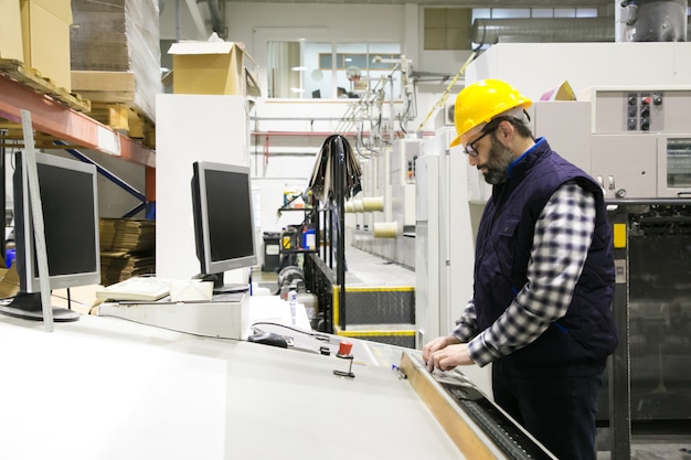 Geconcentreerde mannelijke ingenieur in glazen die machine in werking stellen