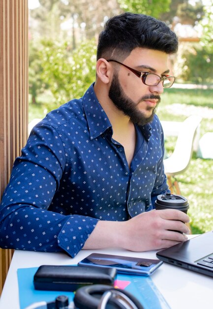 Geconcentreerde mannelijke student die koffie drinkt tijdens het internetten op het terras