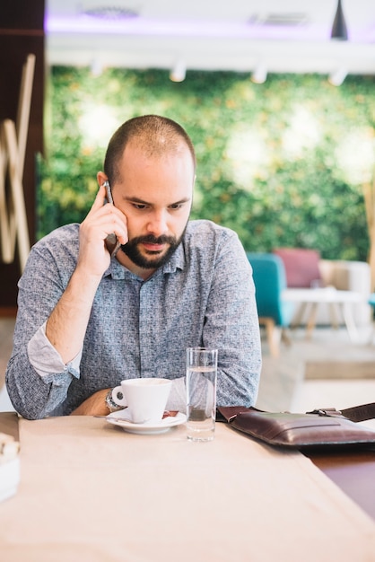 Geconcentreerde mens die op telefoon in koffie spreekt