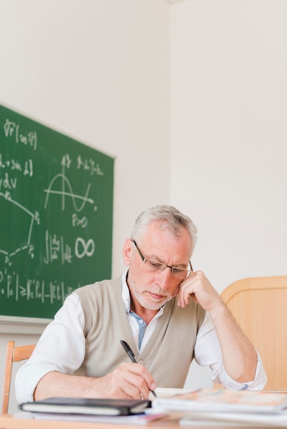 Gratis foto geconcentreerde oude professor die in notitieboekje schrijft